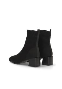 Botas negras hasta el tobillo con textura de punto, con un tacón de bloque y lados elásticos para facilitar su uso. El diseño es minimalista y elegante.