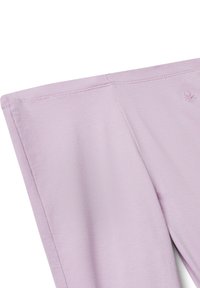 Leggings lilas avec des coutures plates et un petit logo brodé près de la taille sur un fond blanc.