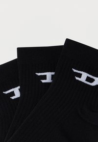 Fekete bordázott zokni fehér logóval a szegélyén, amely közelről mutatja a textúrát és a részleteket.