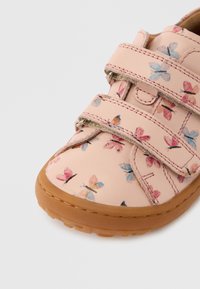 Chaussure en cuir rose avec un imprimé papillon en tons bleus et roses. Dispose de deux bandes Velcro et d'une semelle en caoutchouc marron.