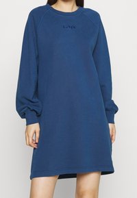 Blaues Sweatshirtkleid mit langen Ärmeln, Rundhalsausschnitt und Logodetail. Weicher Stoff mit lockerer Passform und gerippten Manschetten.