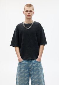Sort ribbet oversized sweatshirt med korte ærmer, båret over lyseblå jeans med et gentaget logomønster. Sølv kædehalskæde tilføjet.