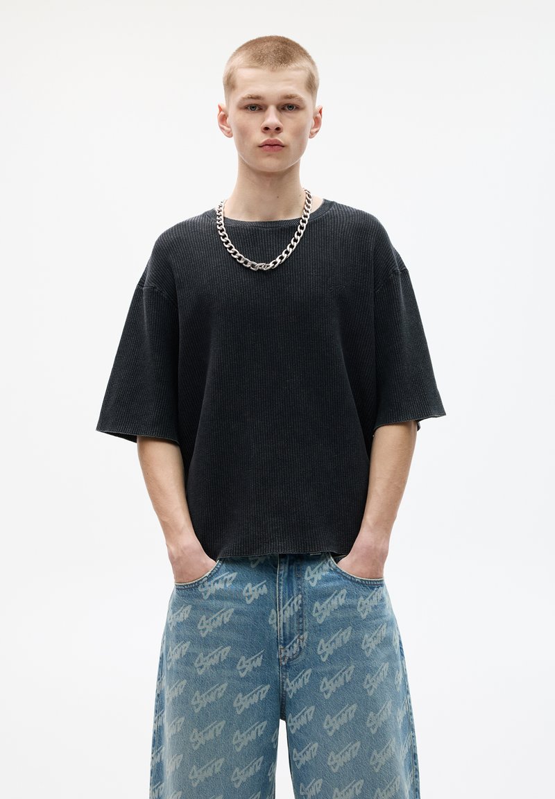 Sort ribbet oversized sweatshirt med korte ærmer, båret over lyseblå jeans med et gentaget logomønster. Sølv kædehalskæde tilføjet.