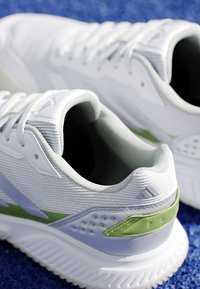 Coppia di scarpe sportive bianche e verde chiaro con suole testurizzate su una superficie blu, mostrando i dettagli posteriori e laterali.