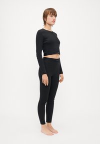 Svart langermet crop top og leggings-sett laget av glatt stoff med en tettsittende design. Begge plaggene har minimal merking på midjebåndene.