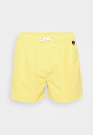 Dzelteni peldbikses vieglā audumā, ar aukliņu jostu un mazu melnu logotipa tagu sānos. Gluda tekstūra, caurspīdīga.