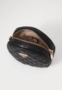 Borsa nera in pelle trapuntata con hardware dorato e chiusura a zip. Interno foderato con etichetta. Forma rotonda, design compatto adatto per gli essenziali.