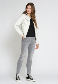 Weißes Leder-Motorradjacke mit Reißverschlusstaschen, kombiniert mit einem schwarzen T-Shirt, grauen, zerrissenen Jeans und schwarzen High-Top-Sneakern.