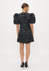 Čierne šaty s vypchatými rukávmi, kvetinovým vzorom, textúrovanou látkou, priliehavým telom a rozšírenou sukňou. Nosené s čiernymi lodičkami.