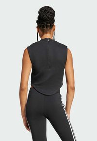 Čierny top bez rukávov s vysokým golierom a zipsom na chrbte, s krátkou siluetou a jemnou textúrou, spárovaný s čiernymi legínami s bielymi pruhmi.