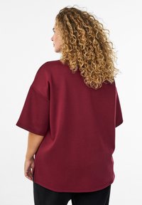 Weinrot oversized Oberteil aus weichem Stoff, mit lockerer Passform, kurzen Ärmeln und seitlichen Schlitzen für zusätzlichen Komfort und Bewegungsfreiheit.