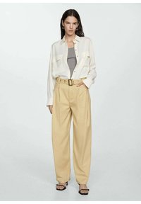 Witte overhemd, grijze tanktop, tan hoge taille broek met riem en zwarte sandalen met bandjes. Soepele texturen, relaxte pasvorm.