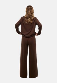 Ensemble composé d'un pull brun à manches longues et d'un pantalon large en tissu doux, présentant une coupe décontractée et une taille élastique pour plus de confort.