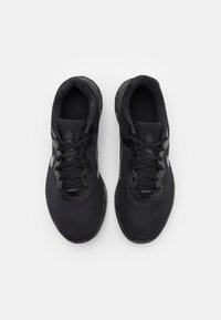 Chaussures de sport noires avec une tige en maille texturée, bout rond, lacets plats et semelle rembourrée. Présente un logo gris sur le côté.