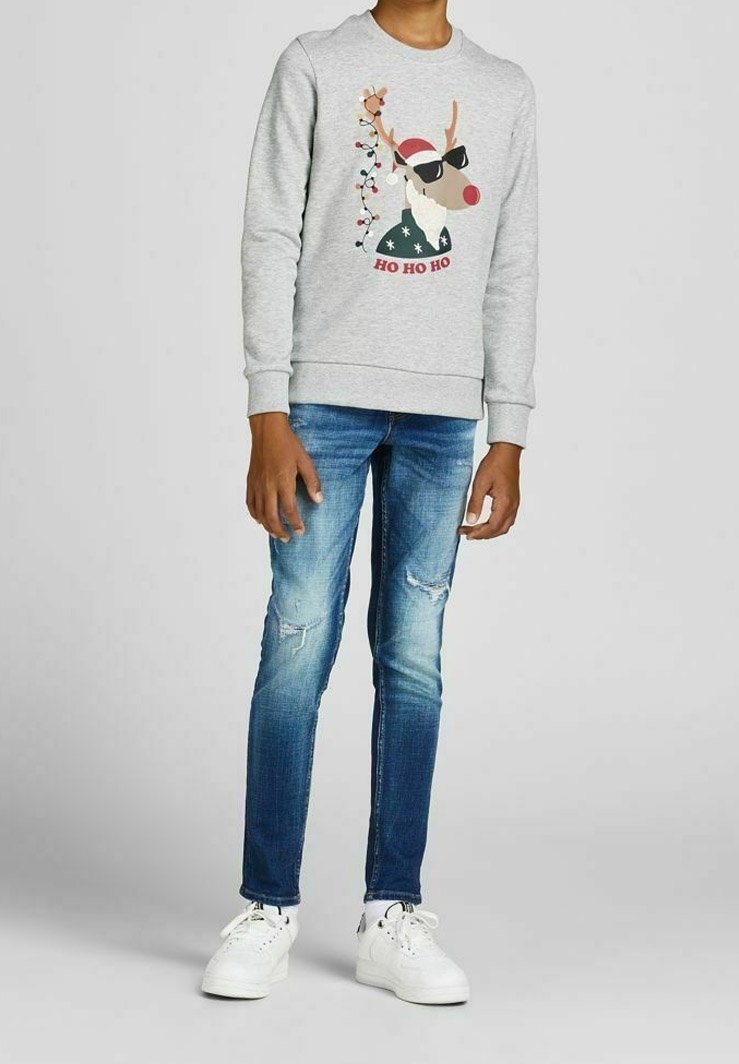 Sweat-shirt gris avec un motif de renne, jean bleu déchiré et baskets blanches. Le design comprend des éléments de Noël et des couleurs vives.