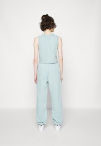 Svetle modrý bezrukávový crop top v kombinaci s volnými kalhotami sladěnými v barvě, vyrobenými z měkkého materiálu, s čistým designem. Bílé tenisky doplňují celkový vzhled.