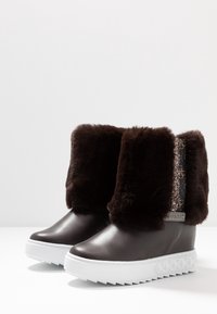 Botines de tobillo de cuero y pelo sintético marrón con suela plataforma de goma blanca y un panel lateral decorativo con patrón.