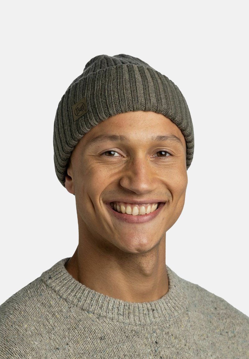 Knit beanie in gray with ribbed texture and turned-up brim; features a small brown label with "Buff" logo. Worn by a smiling individual.