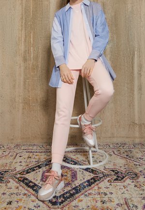 Blå och vitrandig skjorta över en rosa topp, matchad med rosa byxor och vita sneakers med rosa detaljer; sitter på en vit pall.
