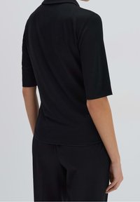 Schwarzes Polohemd mit kurzen Ärmeln und Kragen, glatter Textur, figurbetonter Form und sauberer Naht entlang des Saums und der Ärmel.