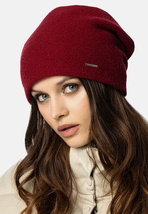 Gorro de punto rojo con una textura suave, diseño holgado y un pequeño acento metálico de marca en el lateral.