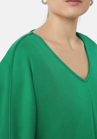 Groene V-hals top met een gladde textuur en een losse pasvorm. Bevat verlaagde schouders en schone stiksels langs de naden.