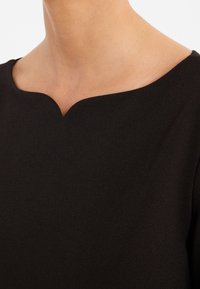 Schwarzes Kleid mit runder Halslinie und glatter Textur. Verfügt über einen leichten V-förmigen Ausschnitt am Kragen, der die Schlichtheit im Design betont.