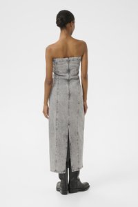 Vestido de denim cinza sem alças com fecho nas costas, costuras verticais e uma fenda até à coxa. Usado com botas pretas de tornozelo.