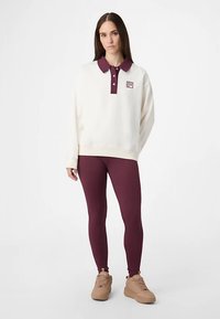 Vit tröja med vinröd krage och liten logga, kombinerad med vinröda leggings och beige träningsskor. Slät tyg, avslappnad passform.