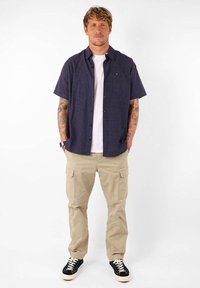 Chemise à manches courtes bleu marine avec des rayures texturées subtiles, associée à un pantalon cargo beige clair et des baskets noires.