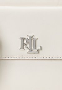 Vit läderväska med en silver "RL"-logotyp, slät yta och prydlig sömnad längs kanterna. Minimalistisk design utan ytterligare mönster.
