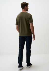 T-shirt in cotone verde oliva con maniche corte, abbinato a pantaloni blu scuro e sneakers blu. Design minimalista, texture uniforme, senza motivi visibili.