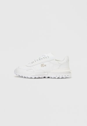 Bela nizka superga z teksturirano podplatjo, vezalkami spredaj in srebrnim logotipom krokodila na strani na enobarvni sivi podlagi.