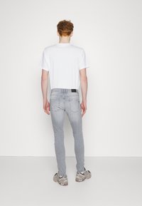 Camiseta blanca de cuello redondo, jeans ajustados de color gris claro y zapatillas grises. Detalles notables incluyen una etiqueta negra en la parte posterior de los jeans.