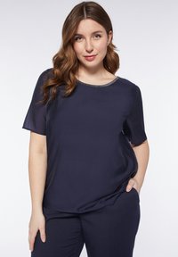 Blusa a maniche corte blu navy con una texture liscia e un collo rotondo decorato con una sottile rifinitura metallica. Adatta per un look casual.