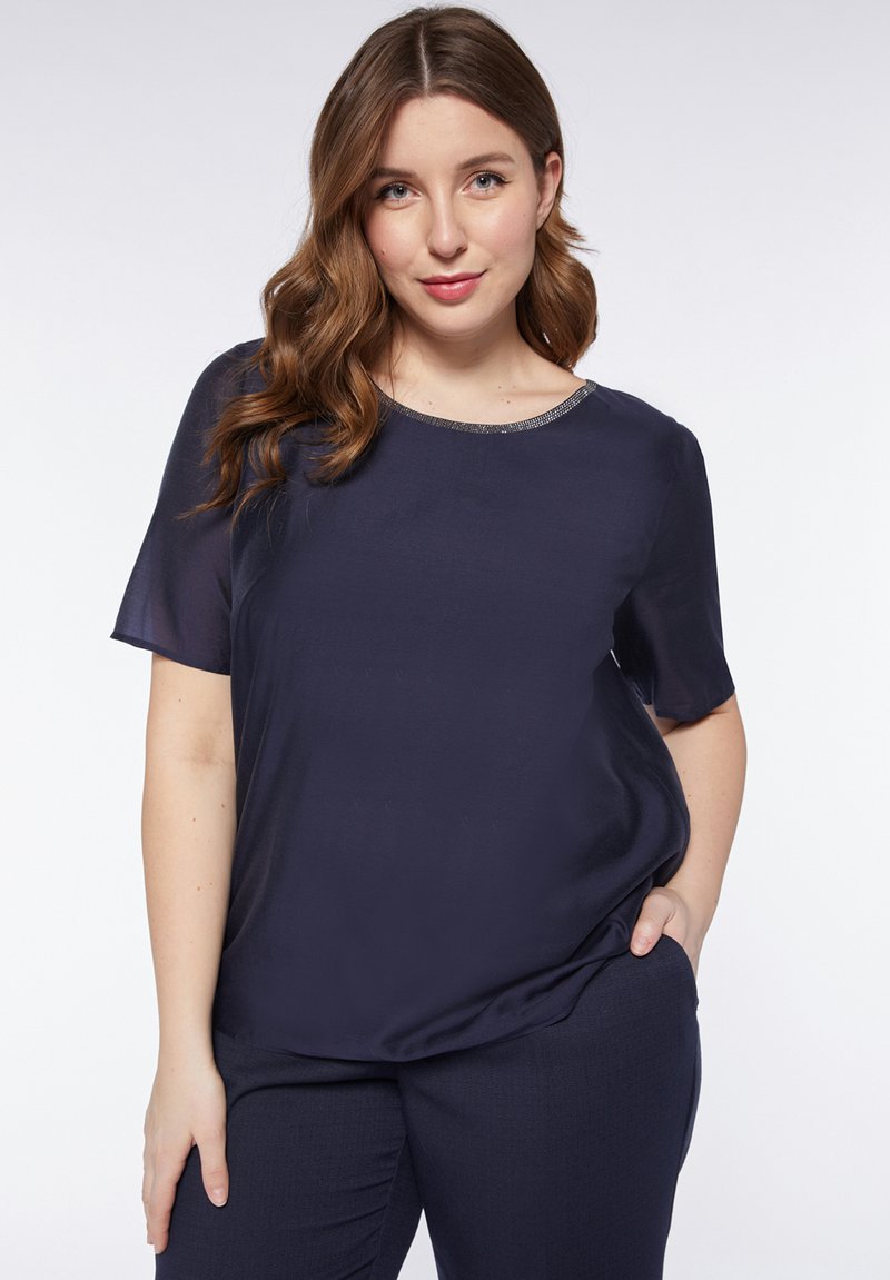 Blusa a maniche corte blu navy con una texture liscia e un collo rotondo decorato con una sottile rifinitura metallica. Adatta per un look casual.