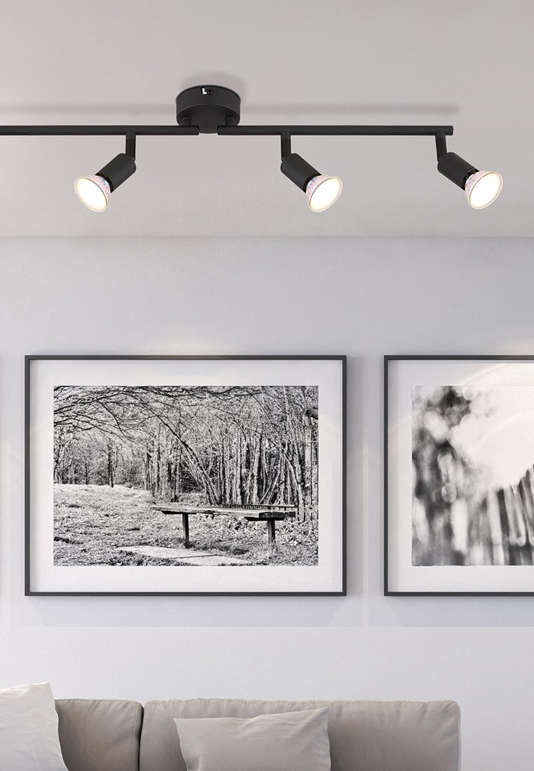 Éclairage sur rail noir avec trois spots réglables, montés au plafond. Présente une finition lisse et un design moderne. Deux photographies encadrées en noir et blanc sur le mur.
