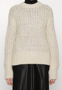 Flauschiger, cremefarbener Strickpullover mit lockerem Geflecht, gerippten Bündchen und Saum. Hat einen Rundhalsausschnitt und eine lockere Passform, die sich von einem schwarzen unteren Teil abhebt.