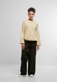 Felpa oversize beige con spalle cadenti, caratterizzata da un delicato logo bianco. Abbinata a pantaloni neri a vita alta e larghi.