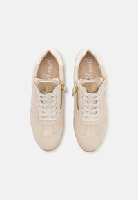 Beige suede sneakers med rund tå, med en gullfarget glidelåsdetalj og kontrasterende snøring. Myk tekstur med et minimalistisk design.