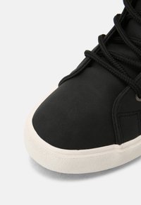 Schwarze Sneakers mit einer glatten, strukturierten Oberfläche und runder Zehenpartie, schwarzen Schnürsenkeln und einer kontrastierenden weißen Gummisohle.