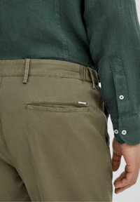 Khaki spodnie z teksturowanym splotem, z płaską tylnią kieszenią i srebrnym akcentem. Połączone z ciemnozieloną koszulą z guzikami na rękawach.