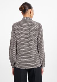 Čierne a krémové vzorované blúzku s dlhými rukávmi, gombíkovými manžetami a klasickým golierom; hladká tkanina s geometrickým dizajnom.