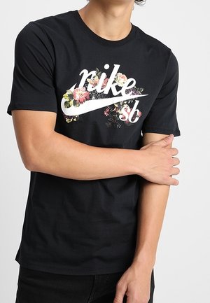 Czarna bawełniana koszulka z białym logo "Nike SB" ozdobionym kwiatowymi akcentami w kolorach różowym, żółtym i zielonym. Krótkie rękawy i okrągły dekolt.