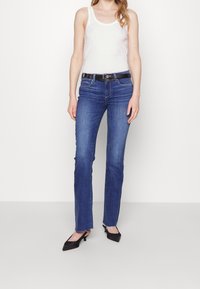 Siniset farkut, joissa on kapea malli, klassinen viisi-taskumalli ja repeytynyt helma, yhdistetty valkoisen toppin ja mustan vyön kanssa.