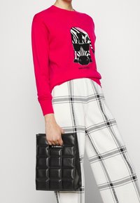 Różowy sweter w gorącym odcieniu z grafiką zebry i czarnymi akcentami, zestawiony z białymi i czarnymi szerokimi spodniami w kratę oraz czarną pikowaną torebką.