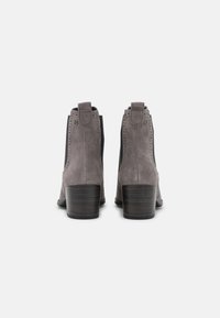 Botas de tobillo de ante gris con tacón cuadrado, paneles laterales elásticos y perforaciones decorativas. Con cordón en la parte trasera para facilitar el uso.