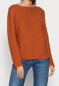 Textured orange sweater with a wide, rounded neckline and long sleeves, paired with blue denim jeans.