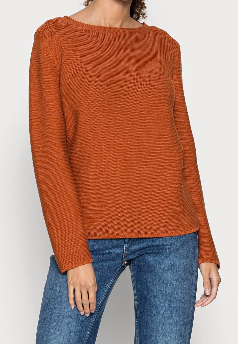 Textured orange sweater with a wide, rounded neckline and long sleeves, paired with blue denim jeans.