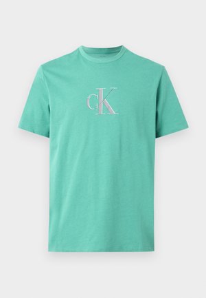 Camiseta turquesa de manga corta con cuello redondo y logo "cK" blanco y a rayas centrado en el pecho.